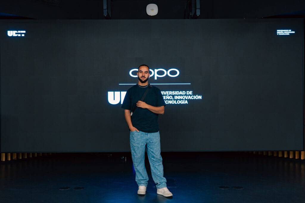 Una persona de pie frente a una pantalla con el logotipo de una universidad sobre un fondo oscuro.