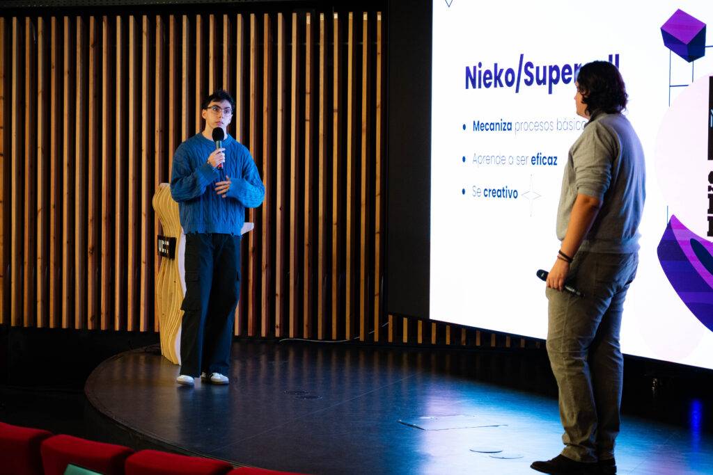 Una presentación en un evento con dos personas en un escenario y una proyección en la pantalla.