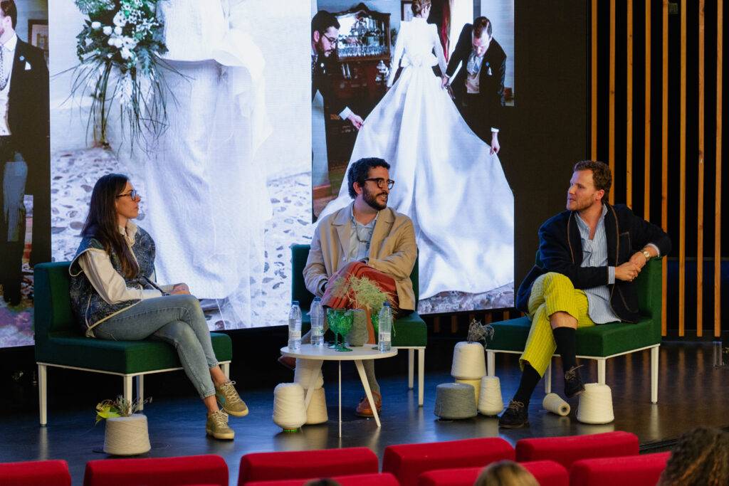 Un panel de discusión con tres personas sentadas en un escenario, entre imágenes de bodas de fondo.