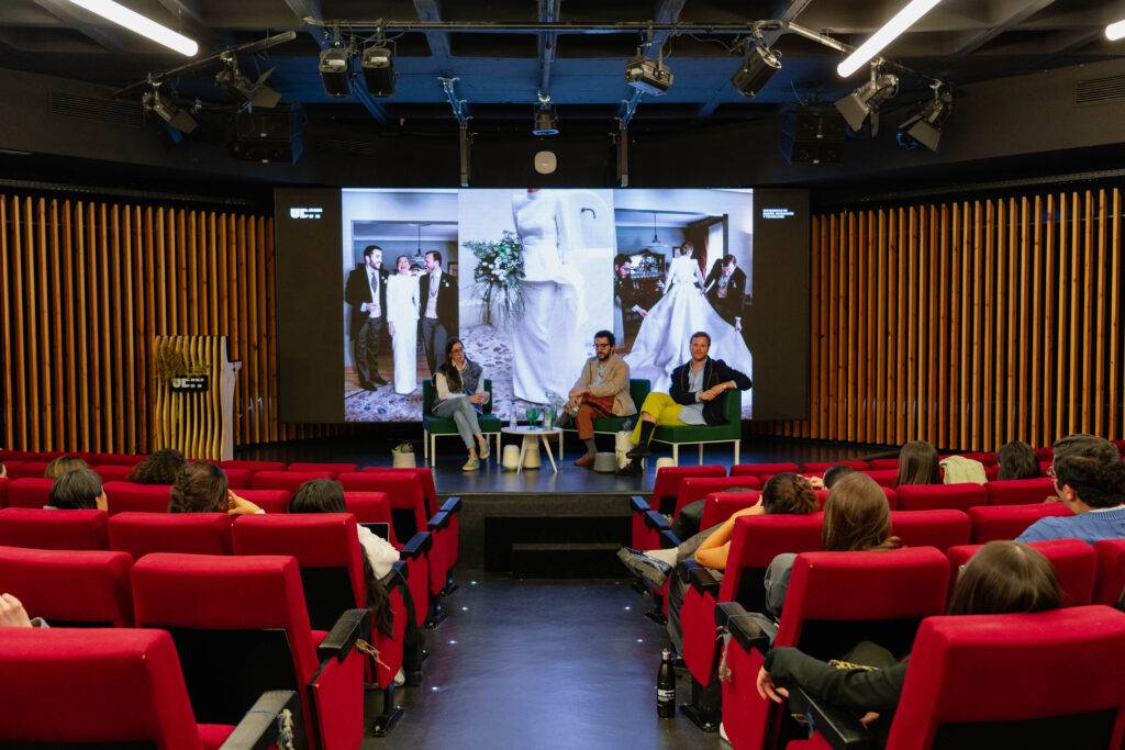 Un grupo de personas asiste a una charla en un auditorio moderno con imágenes proyectadas en la pantalla.