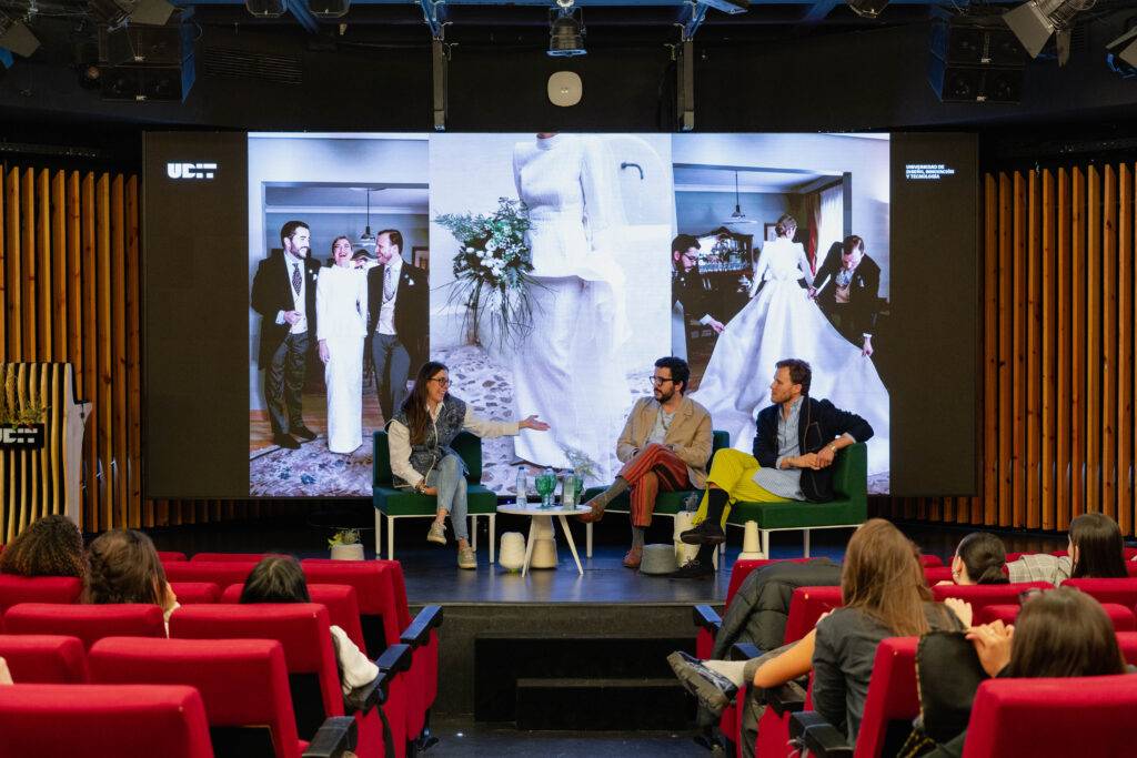 Un panel de discusión en un auditorio con un fondo que muestra una imagen de una boda.