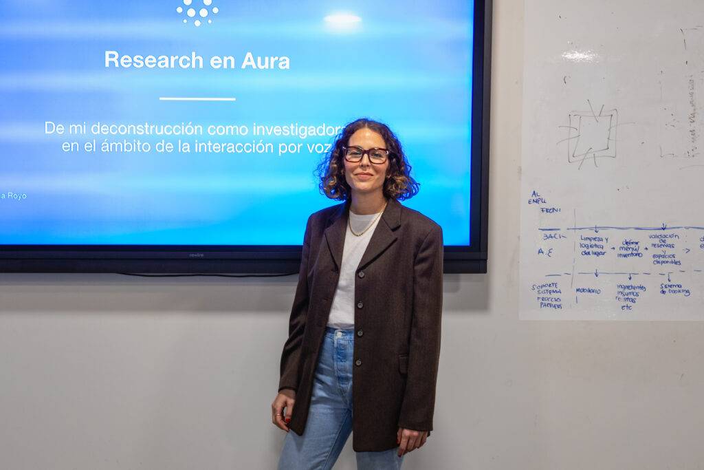 Una persona de pie frente a una pantalla que muestra una presentación titulada 'Research en Aura'.