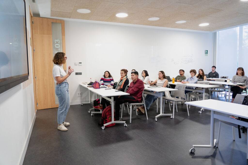 Una persona está dando una presentación frente a un grupo de estudiantes en un aula moderna.