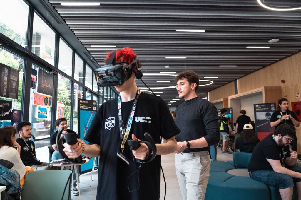 Un joven con auriculares de realidad virtual interactúa con controles mientras otra persona observa en un ambiente moderno.