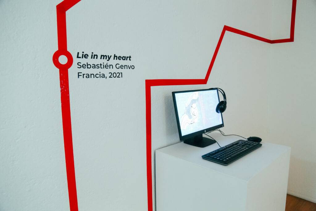 Una instalación artística que presenta una pantalla de computadora con auriculares, acompañada de un texto en la pared que indica el título y el autor de la obra.