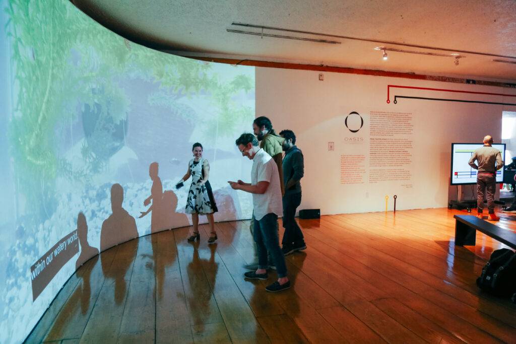 Un grupo de personas interactúa con una proyección en una sala de exposiciones.