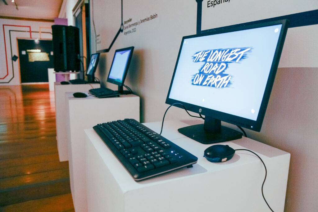 Una exposición con computadoras que muestran el texto 'The Longest Road on Earth'.