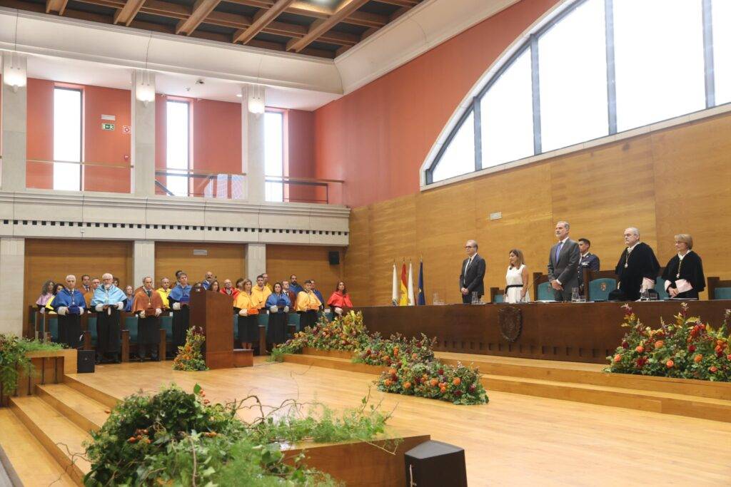 Una ceremonia oficial con varios participantes en un salón decorado con flores y banderas.