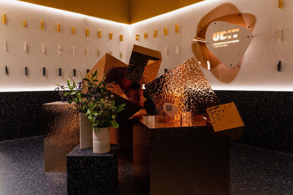 La imagen muestra un espacio interior moderno con objetos decorativos brillantes y un arreglo floral en un jarrón.
