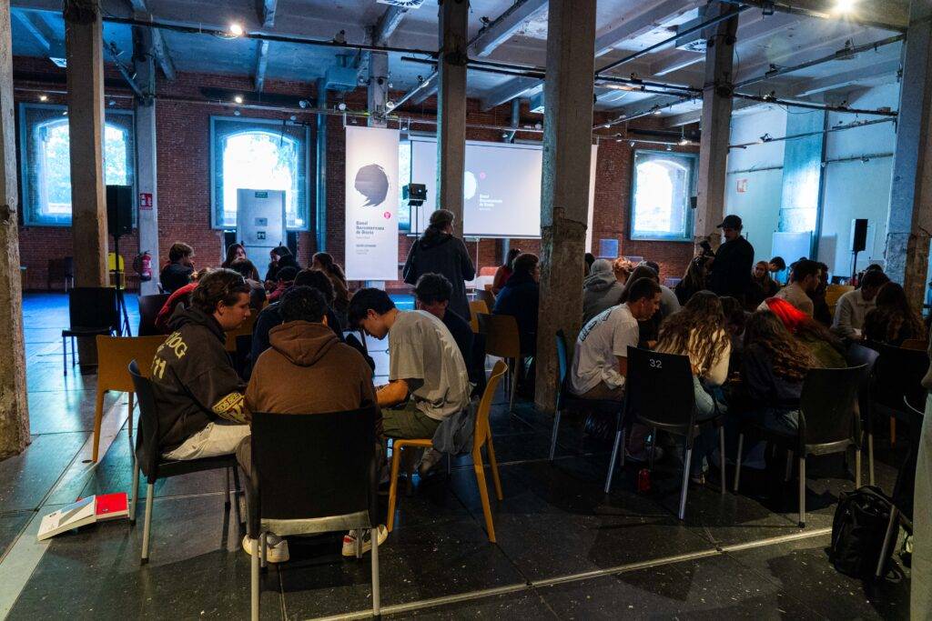 Un grupo de personas se reúne en un espacio amplio y moderno, con sillas y mesas dispuestas para una actividad colaborativa.