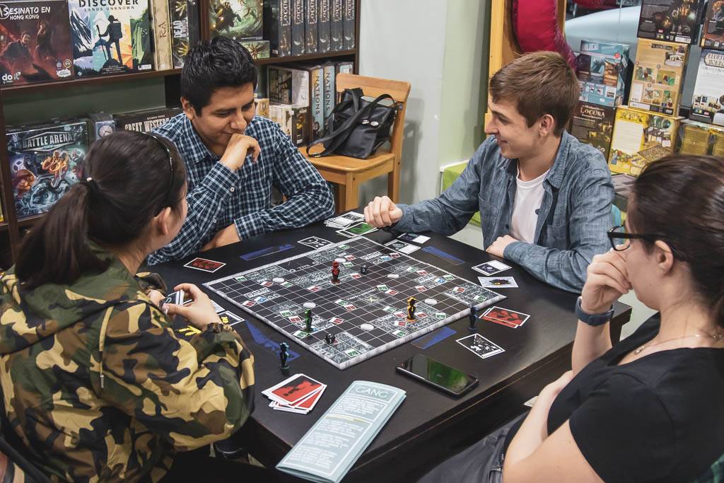 Un grupo de cuatro amigos se reúne alrededor de una mesa para jugar un juego de mesa en una tienda.