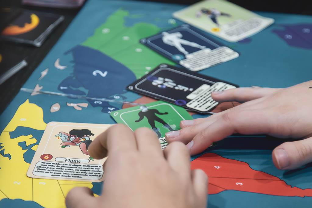 Una persona juega un juego de mesa con cartas sobre un mapa colorido.