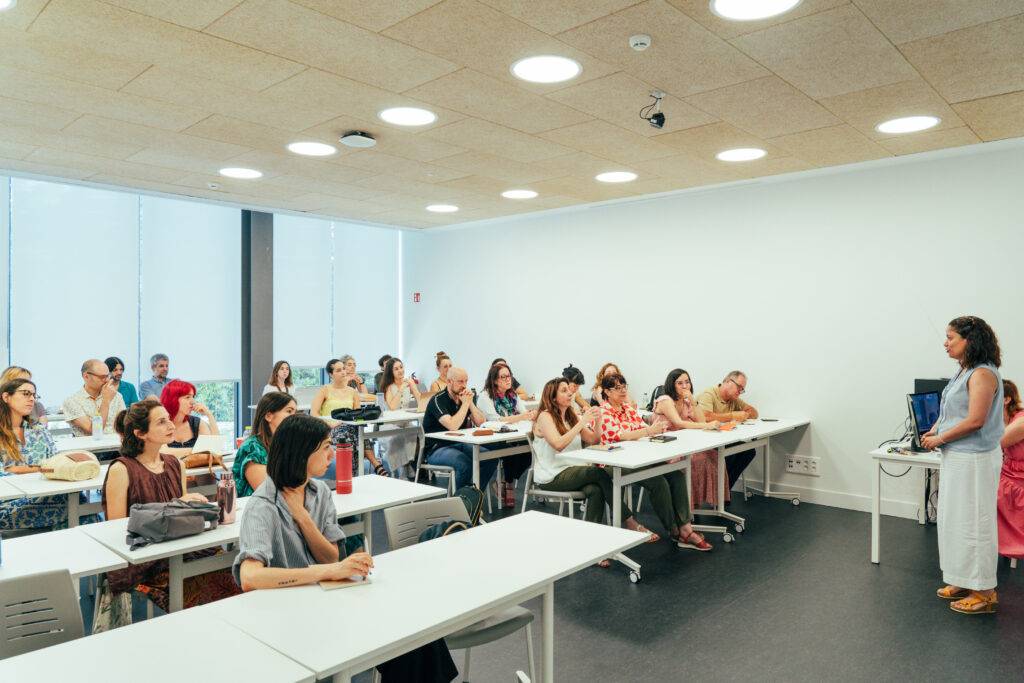 Una sala de clases con numerosos estudiantes atentos a una presentación.