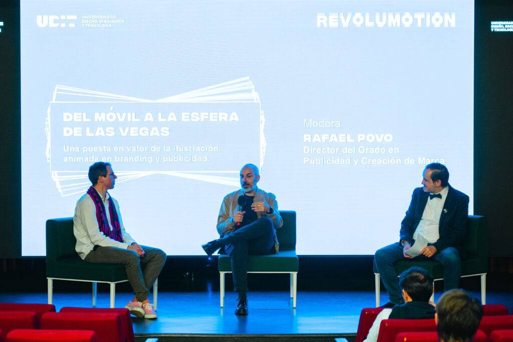 Tres hombres discutiendo en un evento sobre publicidad y comunicaciones en un escenario moderno.