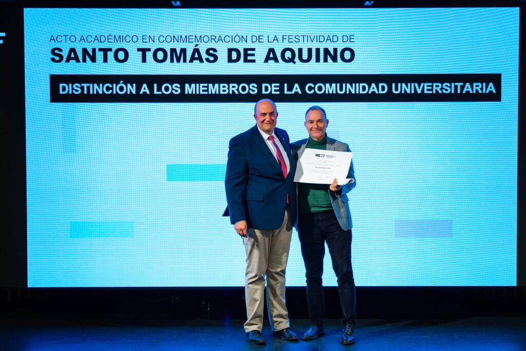 Dos hombres posan juntos en un evento académico, uno de ellos recibiendo un certificado de reconocimiento.