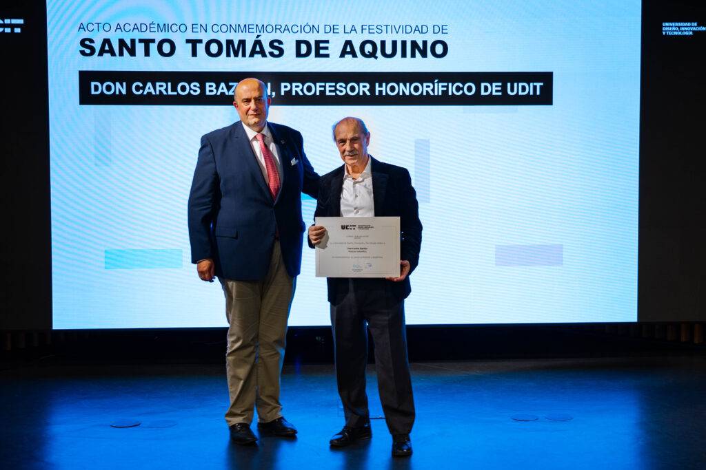 Dos hombres posan en un evento académico en honor a Santo Tomás de Aquino, uno de ellos sosteniendo un certificado.