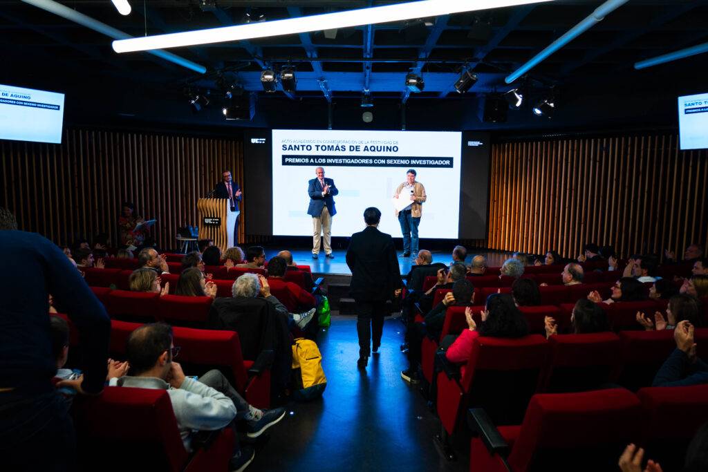 Un evento en un auditorio con personas aplaudiendo mientras dos presentadores están en el escenario.