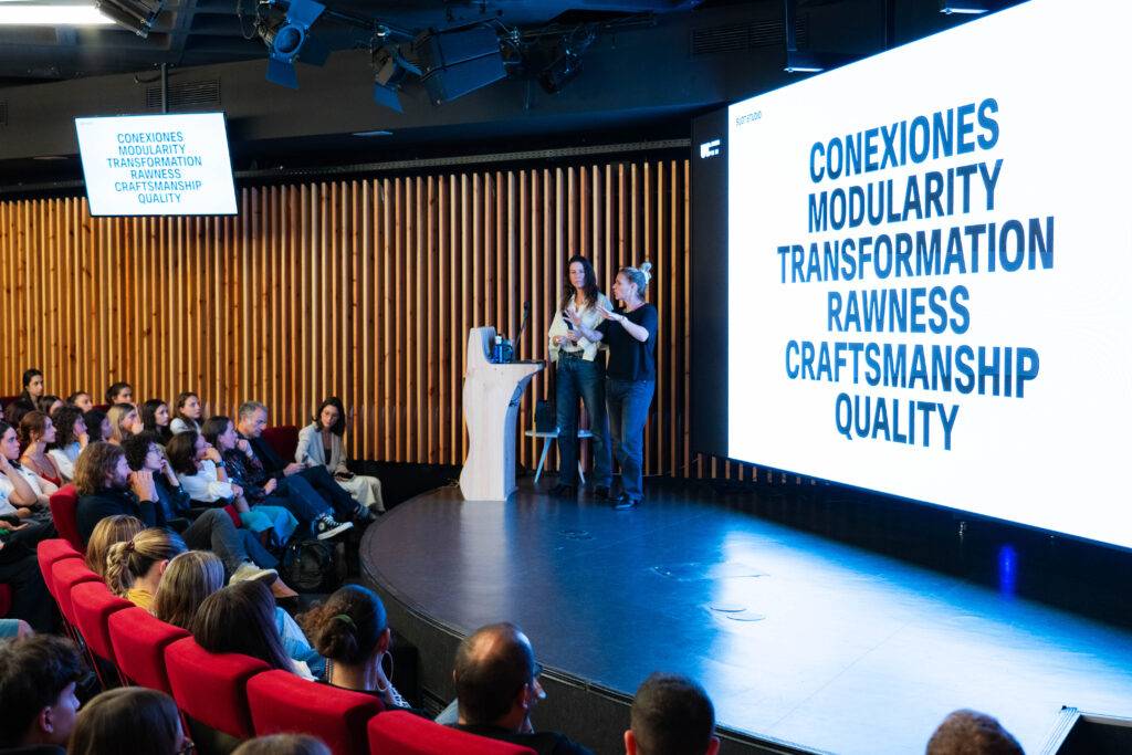 Una presentación en un auditorio con un grupo de personas escuchando y una pantalla que muestra palabras clave relacionadas con la creatividad y el diseño.