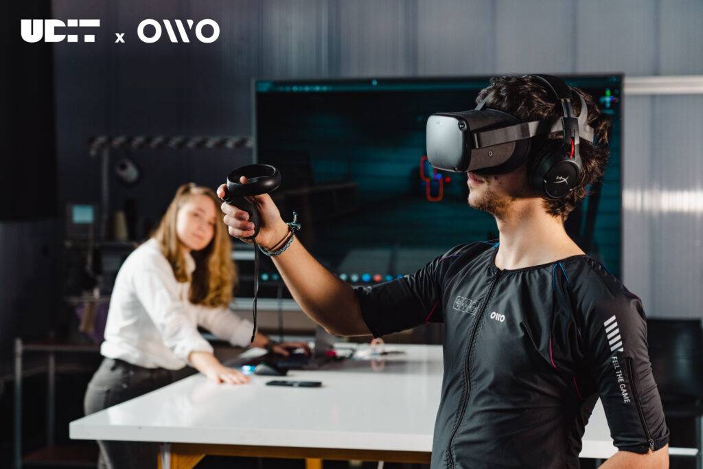 Una persona está usando un visor de realidad virtual y controladores mientras otra persona lo observa en un entorno de trabajo moderno.