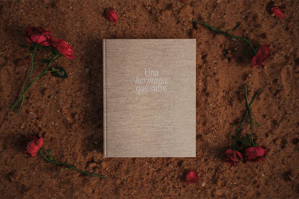 Un libro con una cubierta clara en medio de un fondo de tierra y pétalos de rosa alrededor.