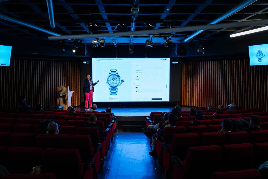Una persona presenta un reloj en una conferencia mientras la audiencia observa.