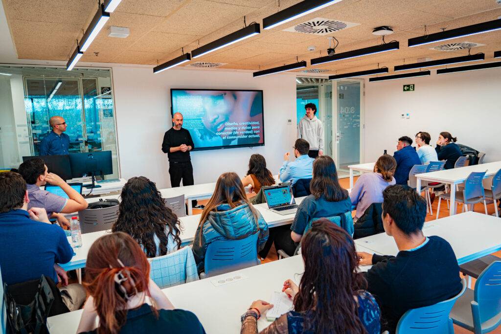 Una sala de clases donde un grupo de personas escucha a un orador frente a una pantalla.