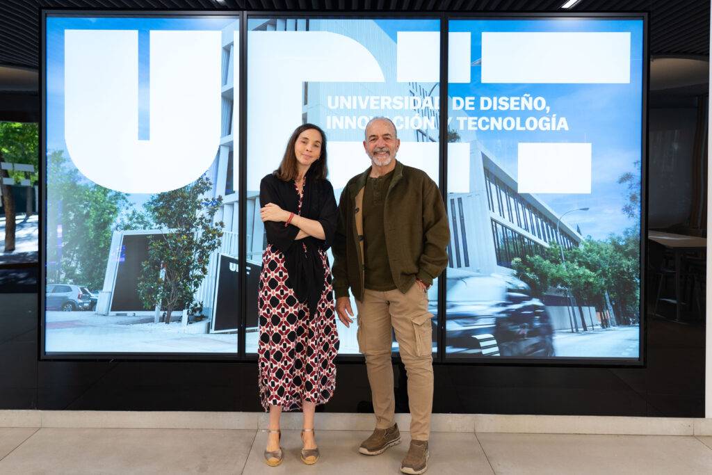 Dos personas posan frente a un gran cartel de la Universidad de Diseño, Innovación y Tecnología.