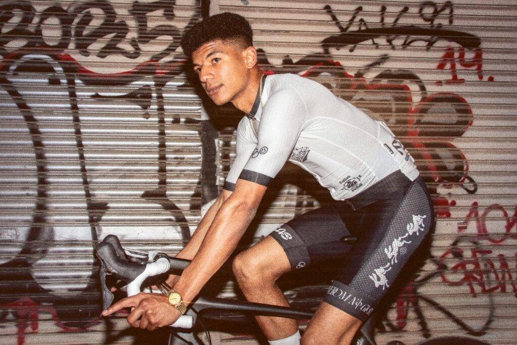 Un joven ciclista posando con su bicicleta frente a un mural grafiteado.