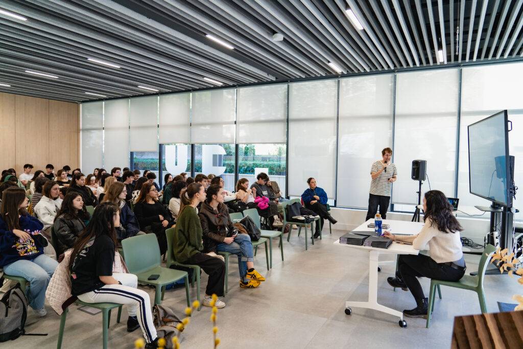 Una sala con un grupo de estudiantes escuchando una presentación frente a una pantalla.