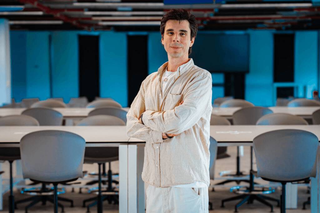 Un hombre con chaqueta clara se encuentra de pie en un espacio de trabajo moderno y vacío.