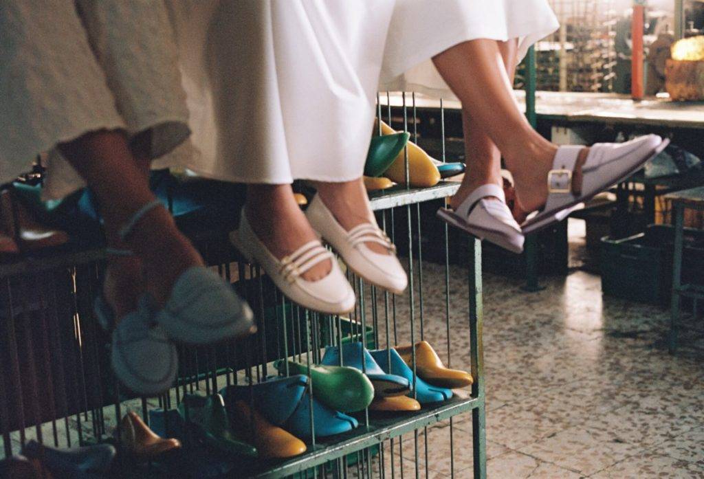 Un grupo de zapatos coloridos exhibidos en estantes, con personas sentadas mostrando sus pies calzando diferentes modelos.