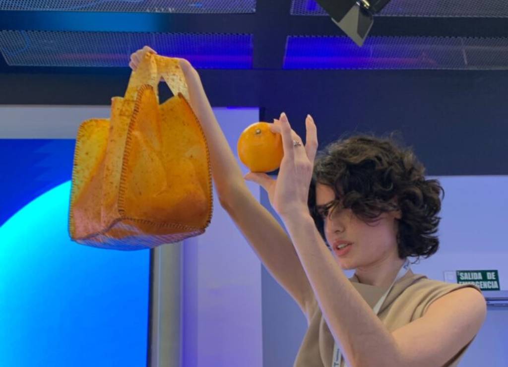 Una mujer sostiene una bolsa naranja y una naranja en un entorno moderno.