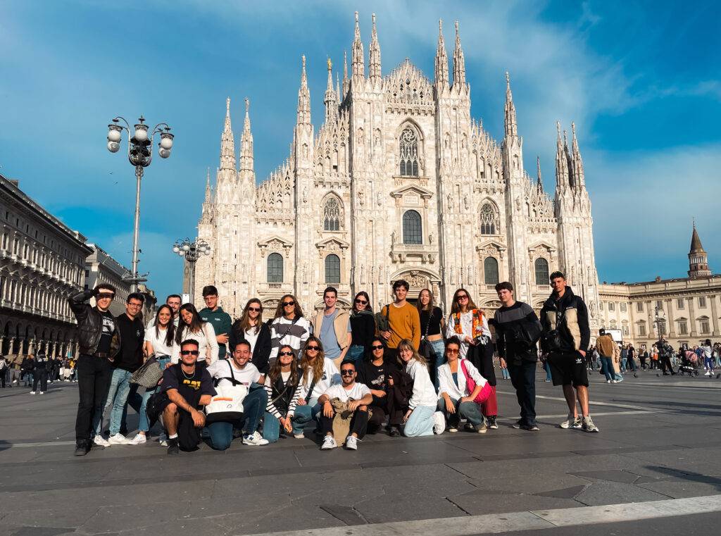 Un grupo grande de personas posa frente a una catedral impresionante en una plaza soleada.