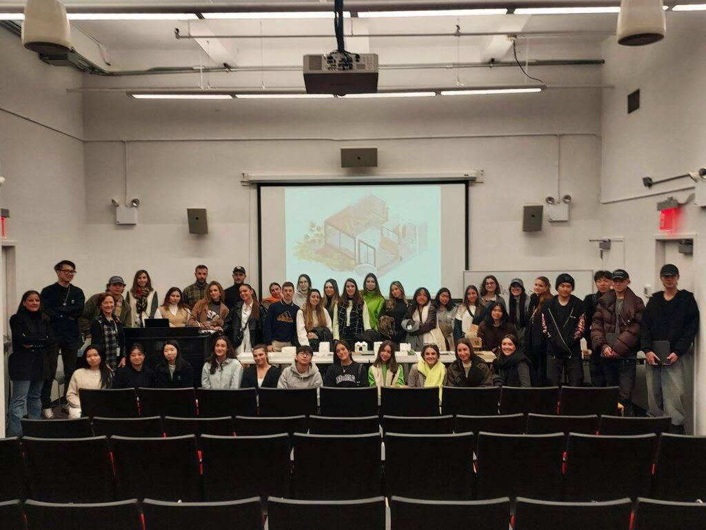 Un grupo de estudiantes posando en un aula con asientos vacíos delante de una proyección.
