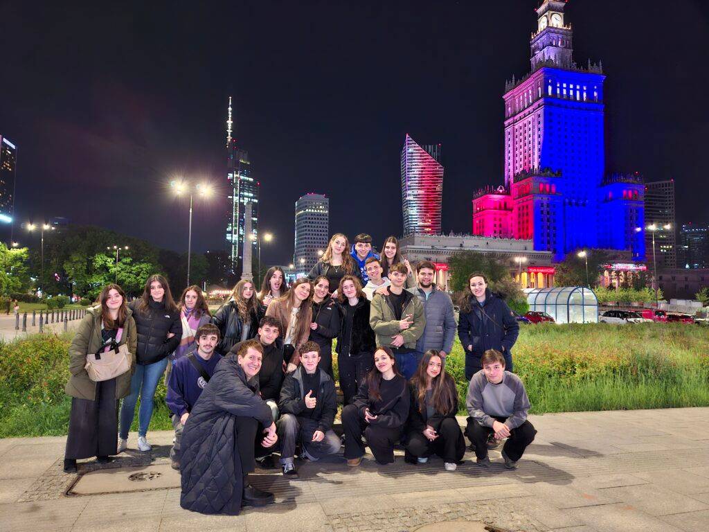 Grupo de jóvenes posando frente a un edificio iluminado de noche en una ciudad moderna.
