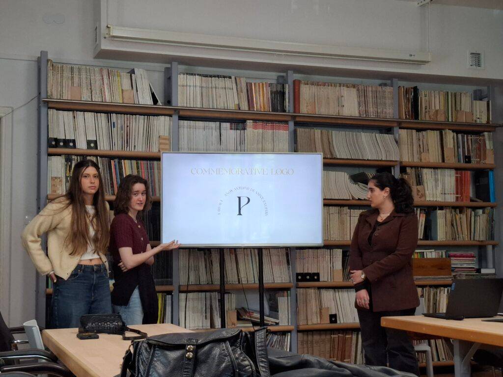 Tres personas presentan un proyecto frente a una pantalla en una sala con estanterías llenas de documentos.