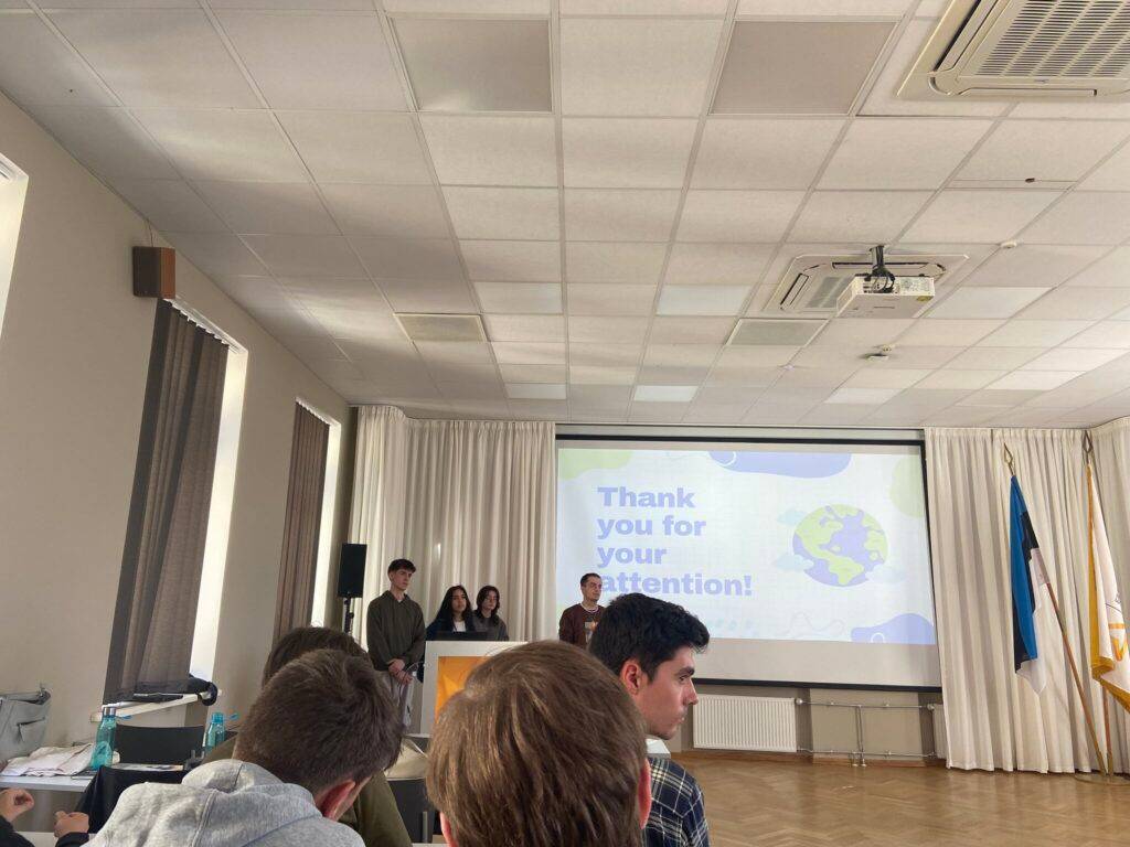Un grupo de estudiantes presenta un proyecto frente a una audiencia en un aula con una proyección en la pantalla.