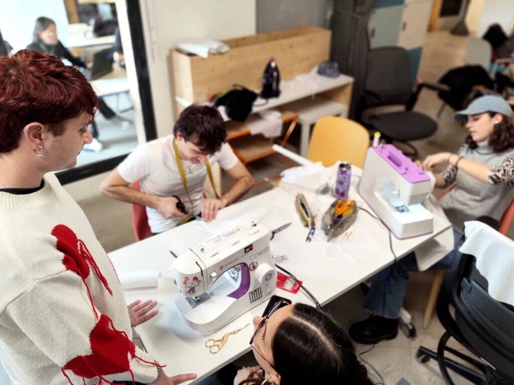 Un grupo de personas trabajando en un taller de costura con máquinas de coser y materiales sobre la mesa.