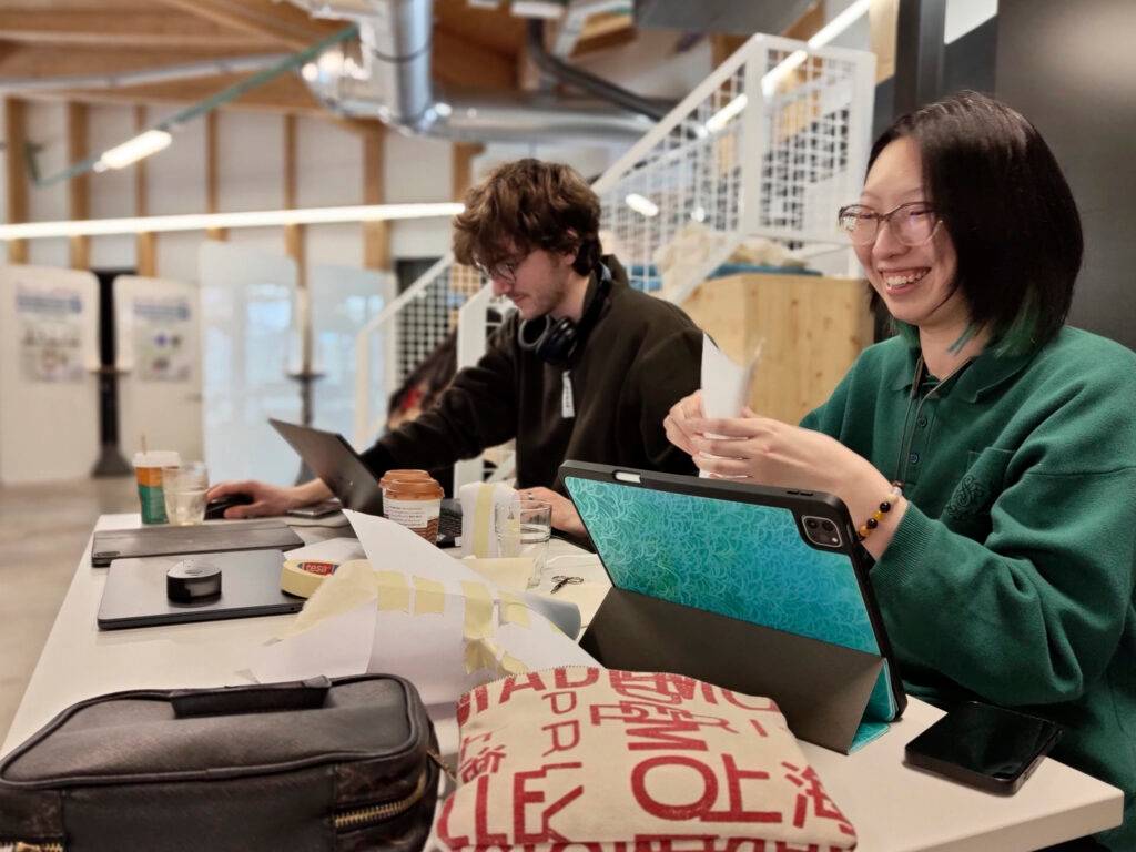 Dos personas trabajando en un ambiente colaborativo, una de ellas sonriendo mientras manipula papel.