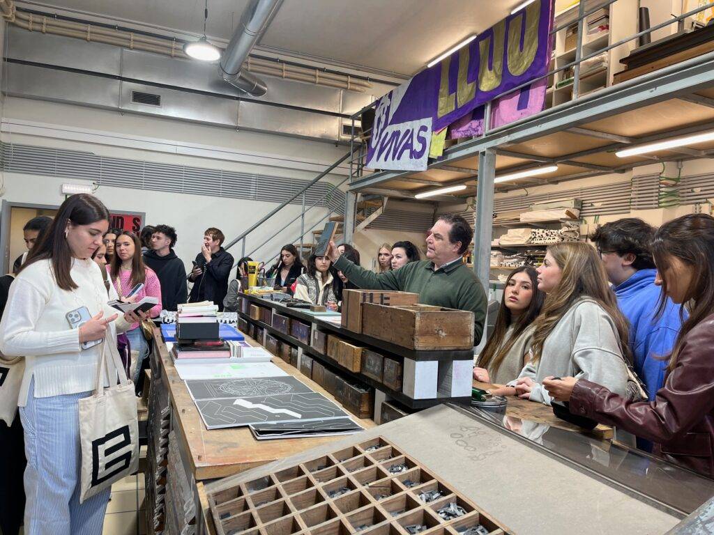 Un grupo de estudiantes interactua en un ambiente educativo mientras un profesor les explica algo en una tienda o espacio de aprendizaje.