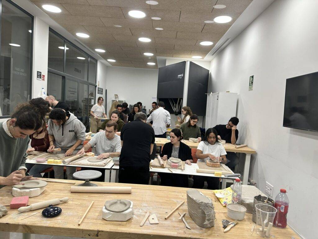 Un grupo de personas trabaja en una clase de cerámica, moldeando arcilla en mesas de trabajo.