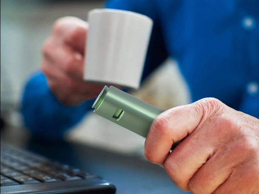 Un hombre sostiene una taza en una mano y un objeto verde en la otra mientras está frente a un teclado.