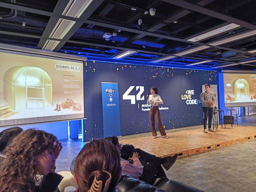 Una presentación en un escenario con dos ponentes, acompañado de una proyección sobre biomedicina.