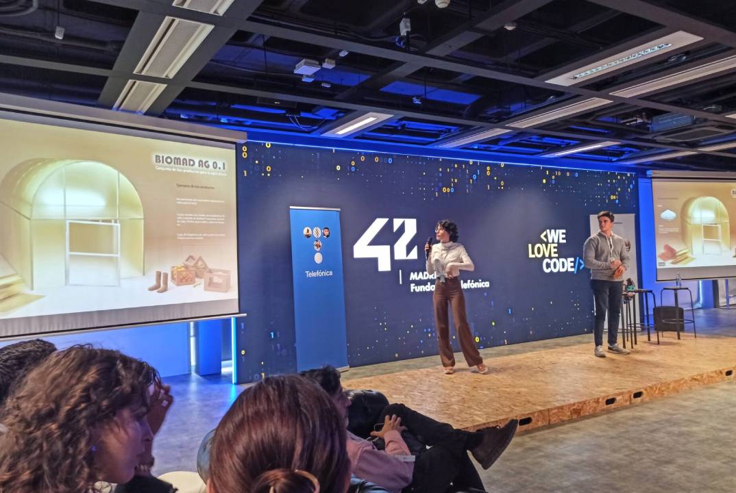 Una presentación en un evento tecnológico con un orador y una presentadora frente a una pantalla.