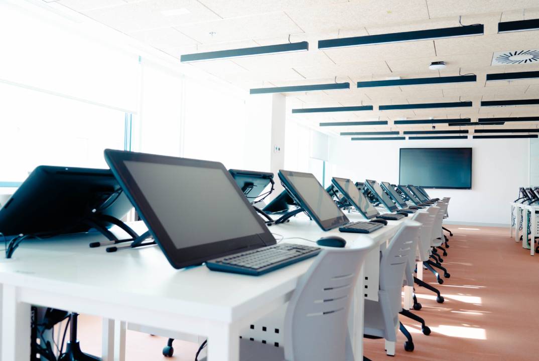 El aula está equipada con varias computadoras en escritorios alineados.