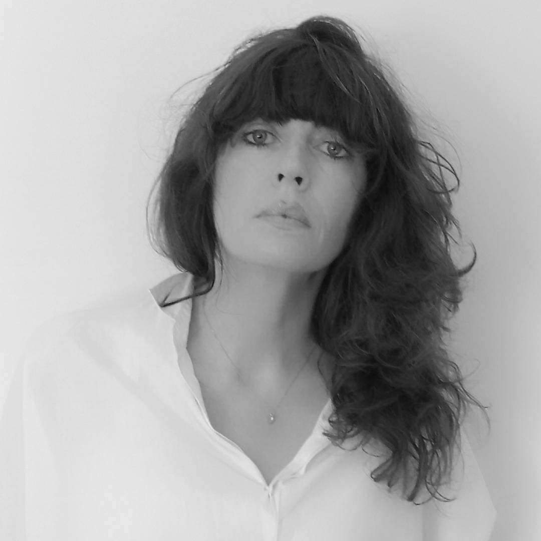La imagen muestra a una mujer con cabello oscuro y un estilo elegante, mirando directamente a la cámara.