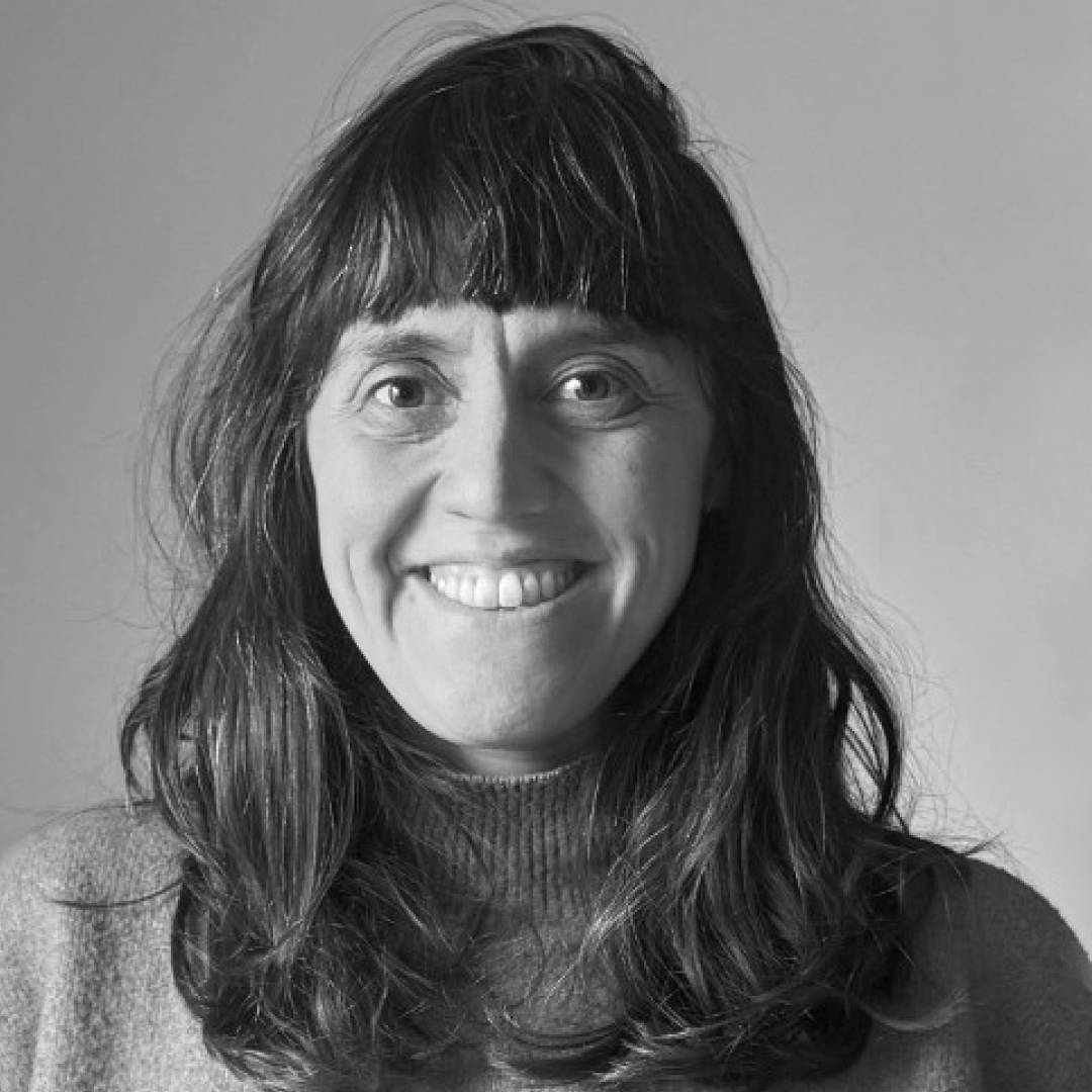 Una mujer sonriente con cabello largo y rizado frente a un fondo claro.