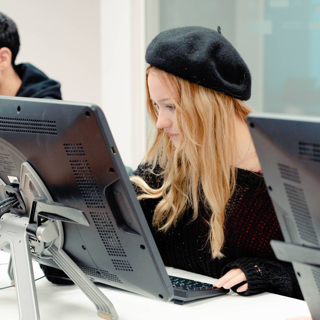 Una joven con un sombrero negro utiliza un ordenador en un entorno de trabajo moderno.