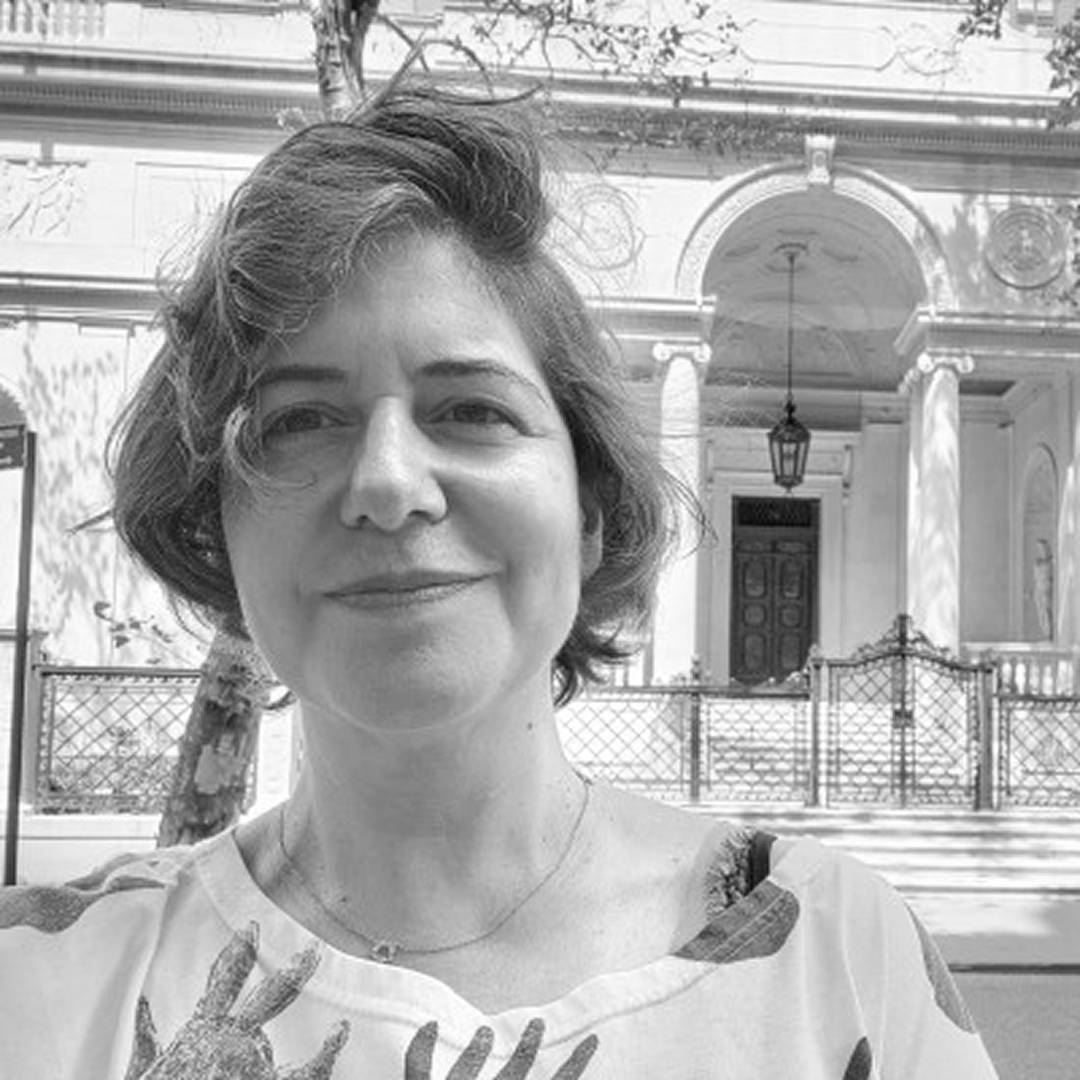 Una mujer sonriente se toma una selfie frente a un edificio clásico.
