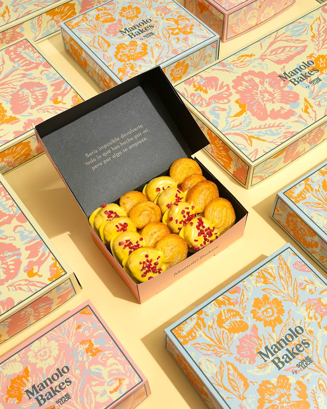 La imagen muestra una caja abierta llena de deliciosos pasteles junto a otras cajas decorativas coloridas.